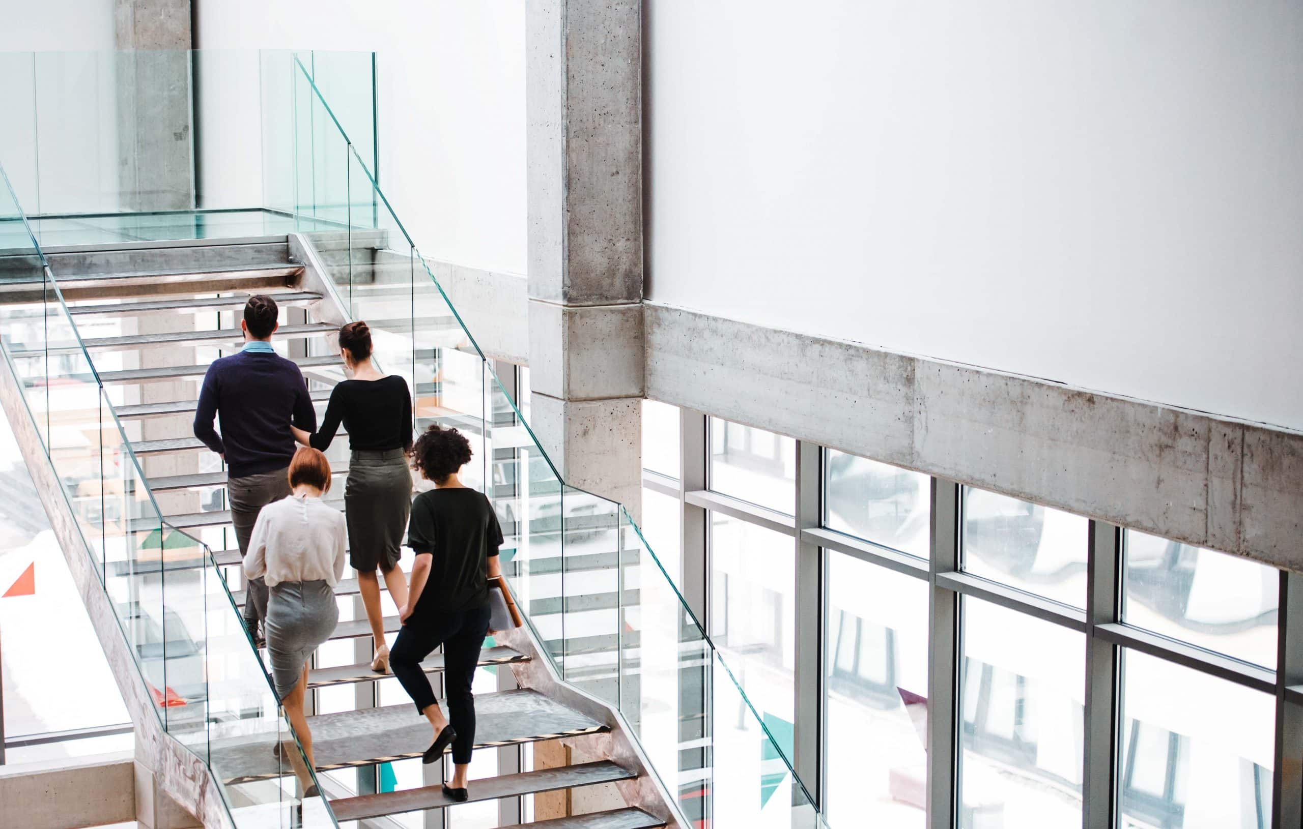 Eine Gruppe von Menschen in Business-Kleidung geht zusammen eine gläserne Treppe hoch